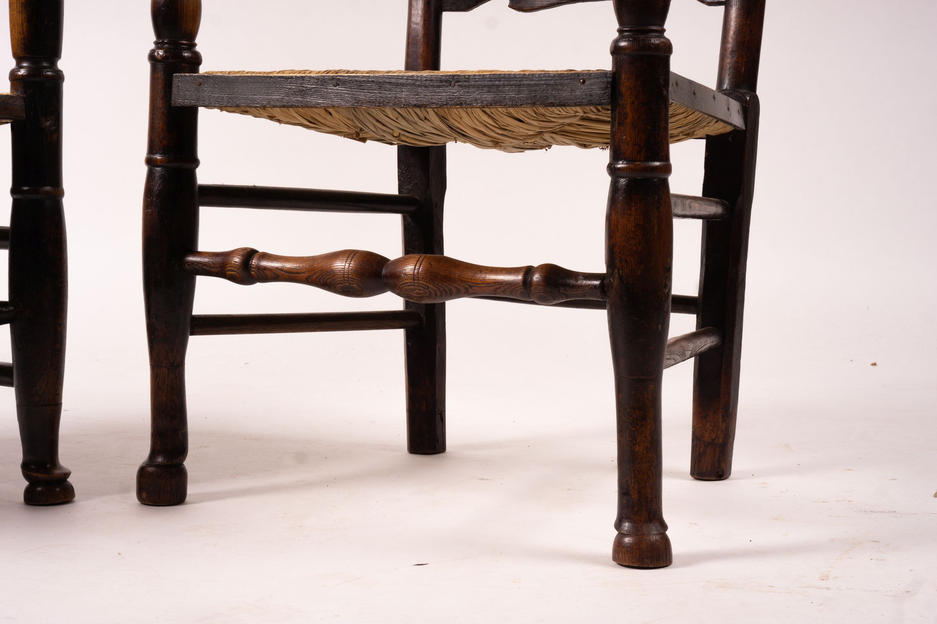 A pair of early 19th century Lancashire ash and fruitwood rush seat ladderback elbow chairs, width 60cm, depth 46cm, height 110cm